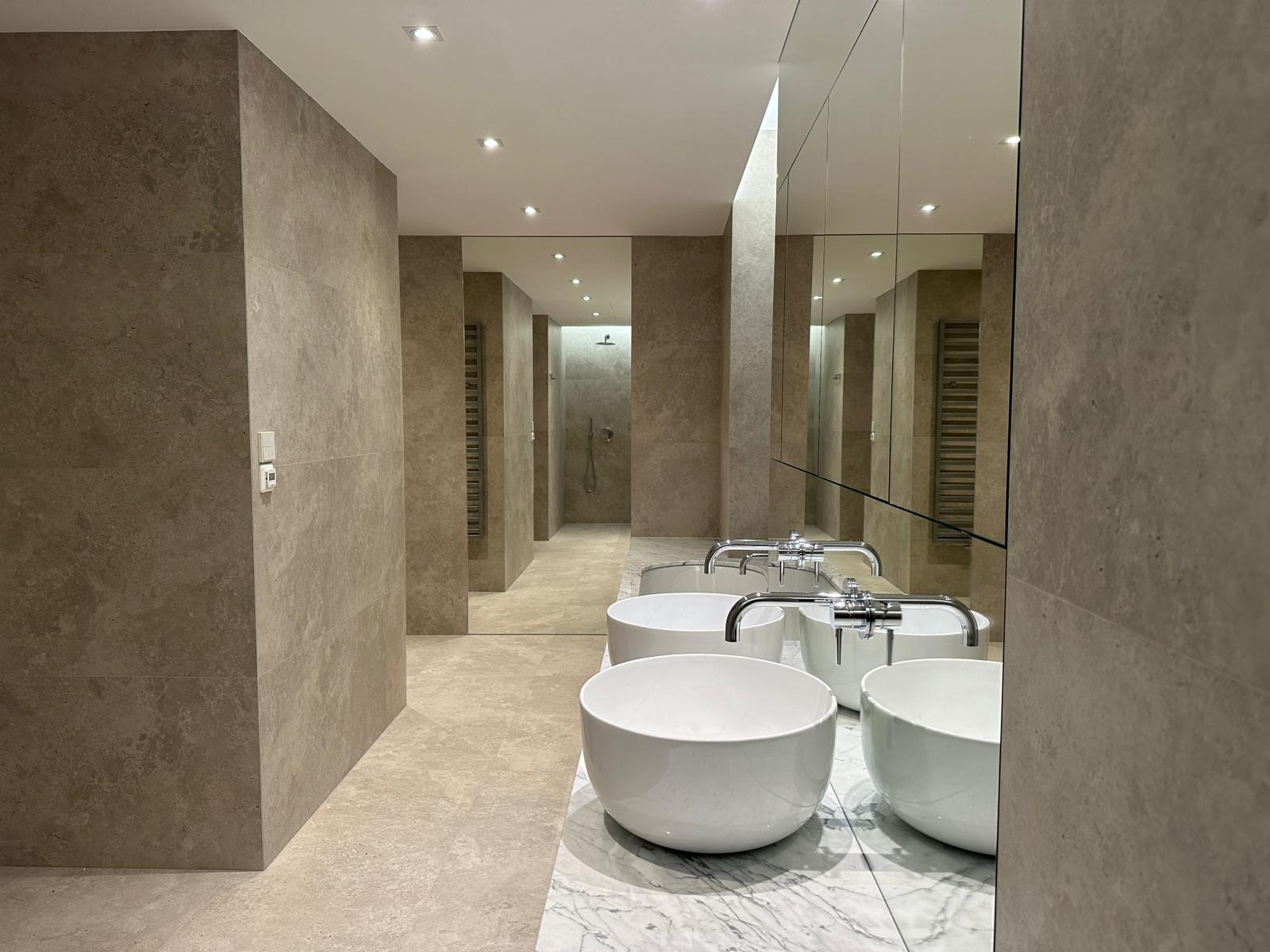 Nowoczesna łazienka w beżowych odcieniach z umywalkami nablatowymi w kształcie mis, marmurowym blatem i dużym lustrem na ścianie.