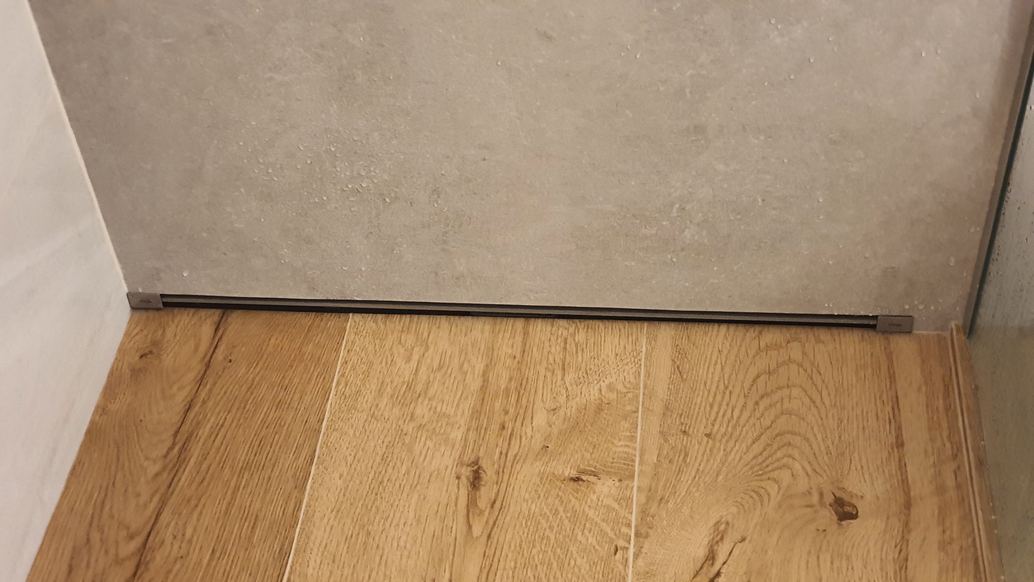 Szczegółowe ujęcie podłogi z paneli i odpływu liniowego w kabinie prysznicowej w Warszawie, widoczne delikatne krople wody na ścianie z płytek.