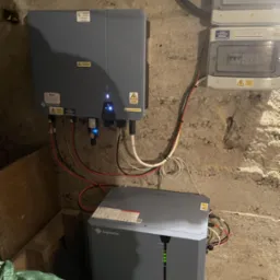 Dwa inwertery Solplanet i rozdzielnice PV-AC i PV-DC zamontowane na surowej, betonowej ścianie w piwnicy; widoczne kable i diody sygnalizacyjne.