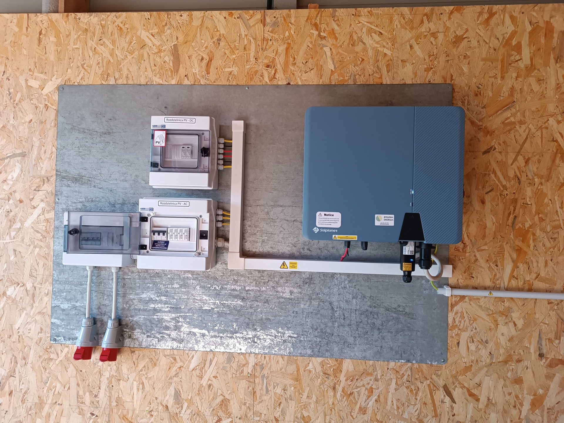 Instalacja fotowoltaiczna: rozdzielnice PV-DC i PV-AC oraz falownik Solplanet zamontowane na metalowej płycie na tle ściany z płyty OSB.