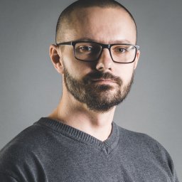 zenPixel - Portret mężczyzny z brodą i okularami na szarym tle. Ujęcie od przodu, skupione na twarzy. Neutralny wyraz twarzy, krótko ostrzyżone włosy.