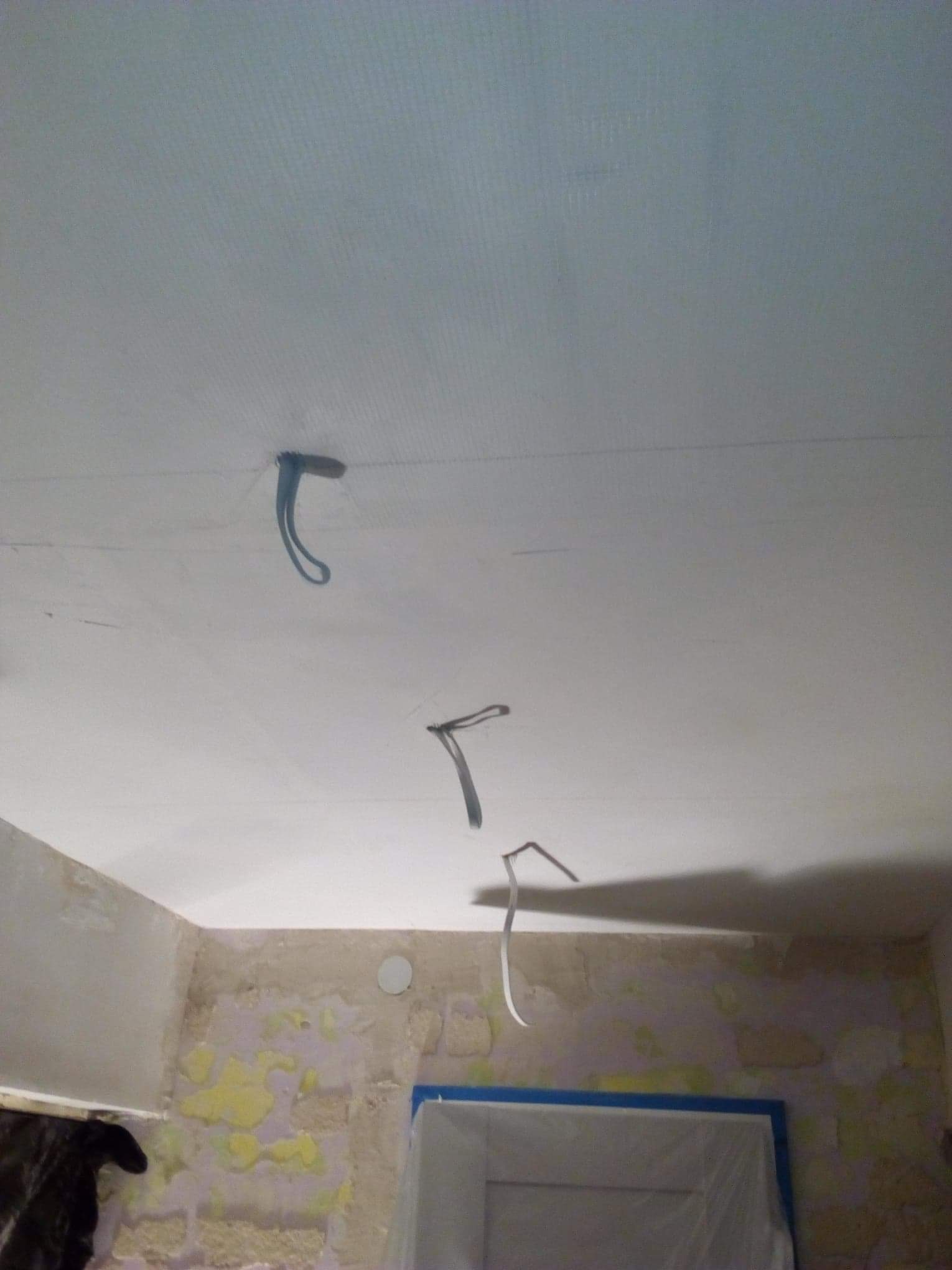 Przygotowanie do montażu oświetlenia: sufit po szpachlowaniu z wystającymi przewodami elektrycznymi, ściany w trakcie usuwania starej farby, okno zabezpieczone folią.