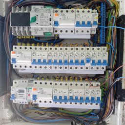 OLEH SHPAKOVSKYI - Rozdzielnica elektryczna z licznymi zabezpieczeniami, przewodami i listwami zaciskowymi, widoczne elementy sterujące i pomiarowe, zainstalowana w białej obudowie.