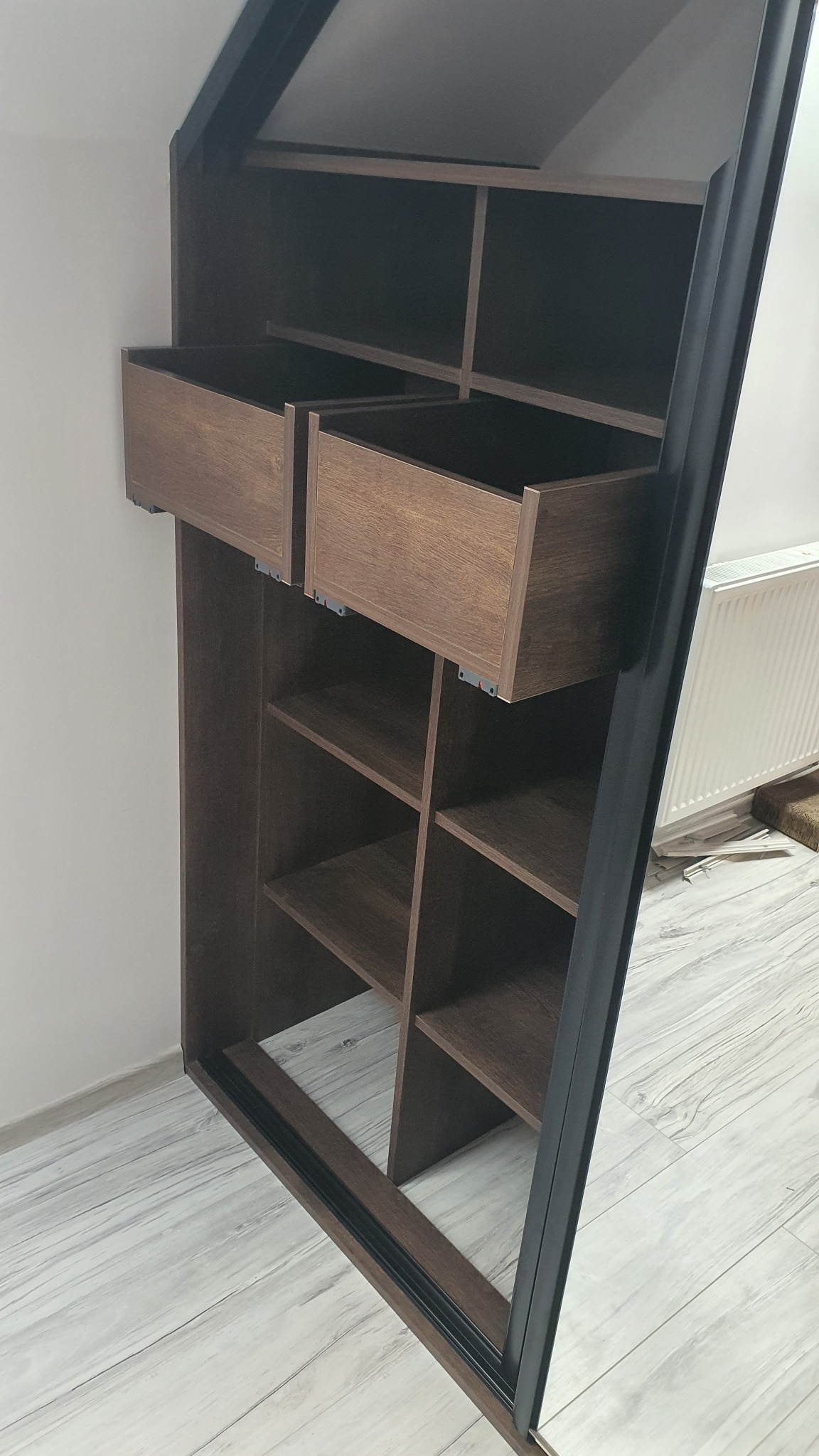 Wnętrze szafy wnękowej z dwoma wysuniętymi szufladami, brązowe drewno, czarna rama, widok z dołu.