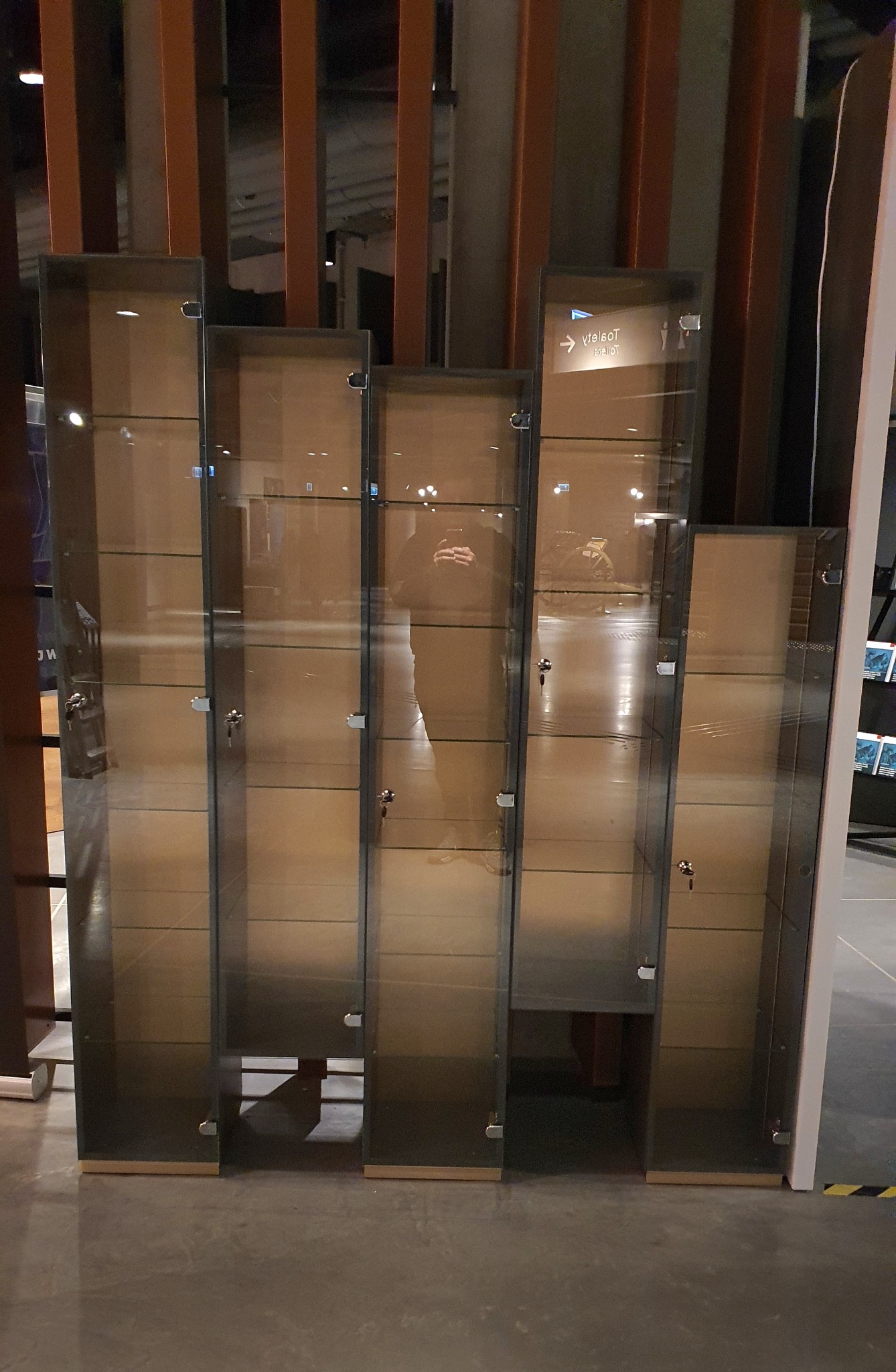 Szereg szklanych witryn ekspozycyjnych z metalowymi ramami i zamkami, o różnej wysokości, ustawionych na szarym tle podłogi.