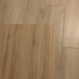 Fragment ułożonej podłogi z paneli w odcieniach beżu, z pojedynczym panelem leżącym obok, ukazującym wzór drewna.