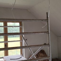 Elizalia Pavlo Tkachuk - Poddasze po montażu płyt G-K, widoczne kable, rusztowanie z narzędziami i oknem w tle. Izolacja z wełny mineralnej przy ścianie szczytowej.