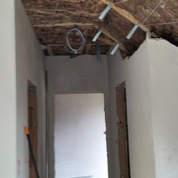 Elizalia Pavlo Tkachuk - Poddasze w trakcie ocieplania wełną mineralną, widoczne metalowe elementy mocujące i przygotowane otwory drzwiowe. Ściany po szpachlowaniu, gotowe do malowania.