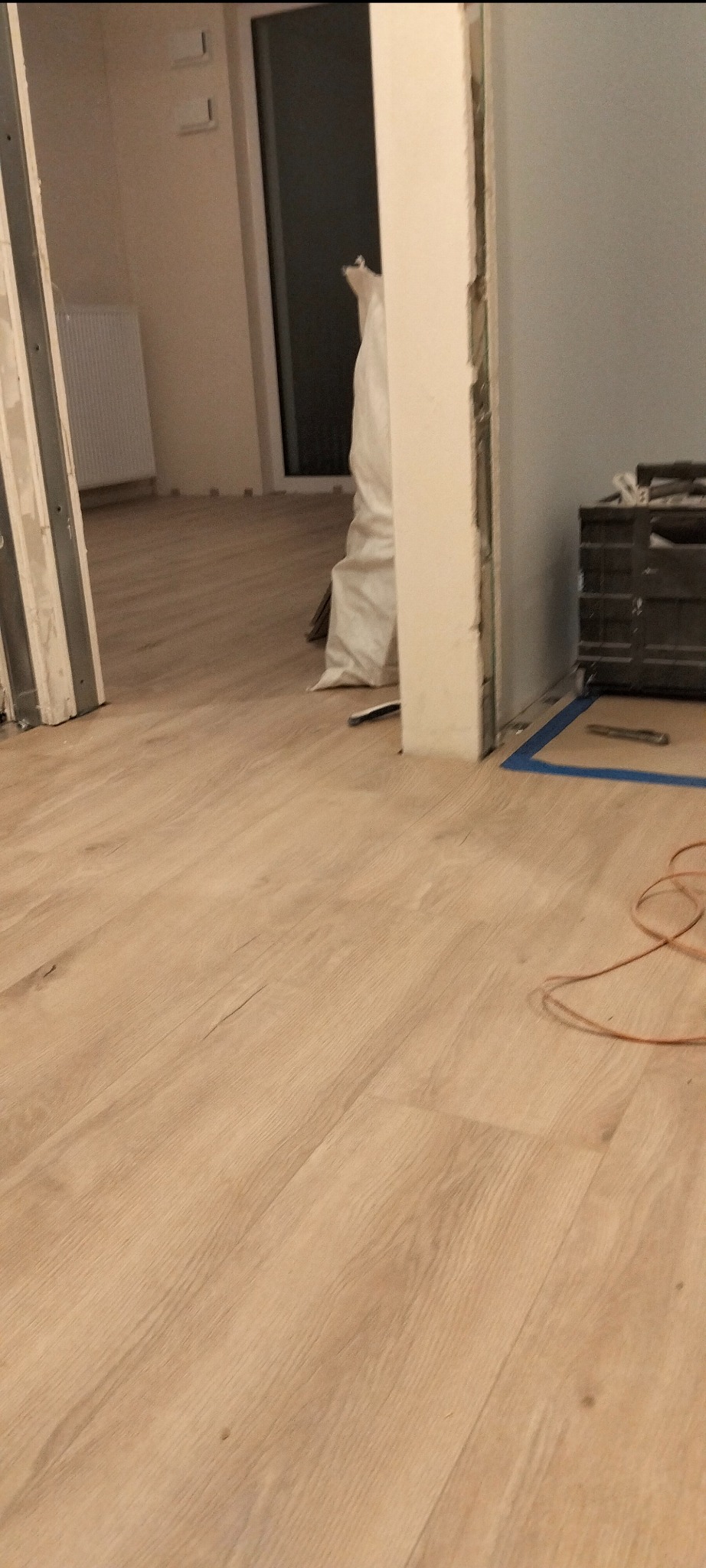 Układanie paneli podłogowych w trakcie remontu, widoczna torba z materiałami budowlanymi, skrzynka narzędziowa i fragment kabla elektrycznego na nowej podłodze.