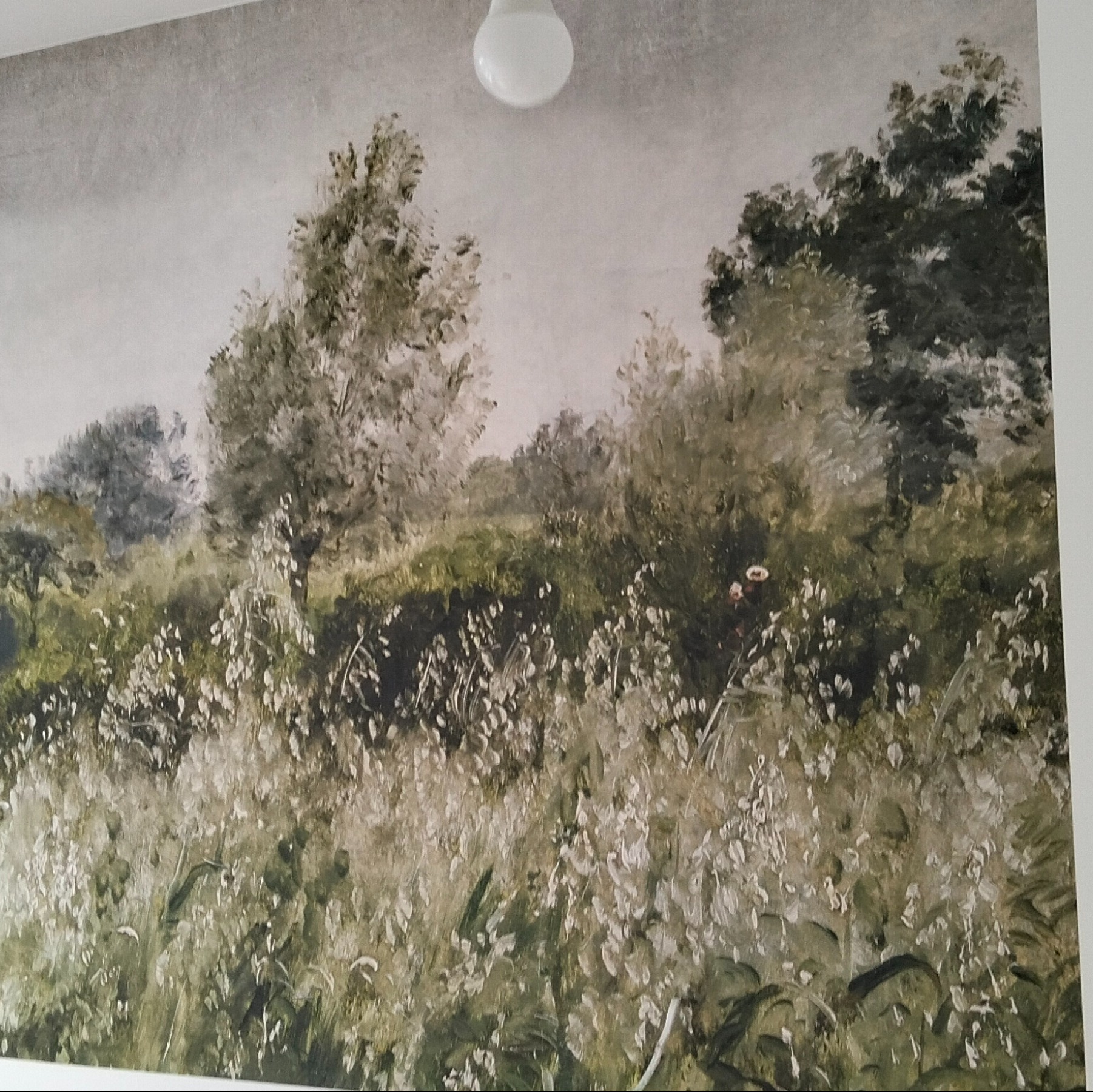 Fototapeta w stylu impresjonistycznym z motywem łąki i drzew, oświetlona przez pojedynczą żarówkę na suficie. Delikatne, rozmyte pociągnięcia pędzla tworzą iluzję głębi.