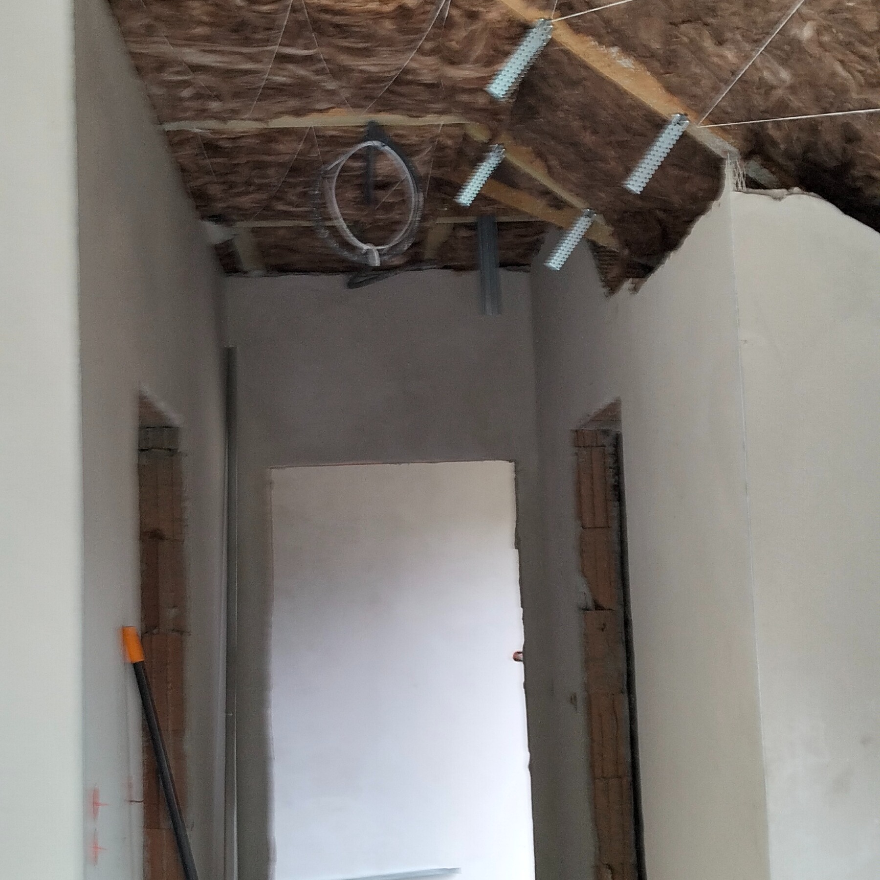 Poddasze w trakcie ocieplania wełną mineralną, widoczne metalowe elementy mocujące i przygotowane otwory drzwiowe. Ściany po szpachlowaniu, gotowe do malowania.