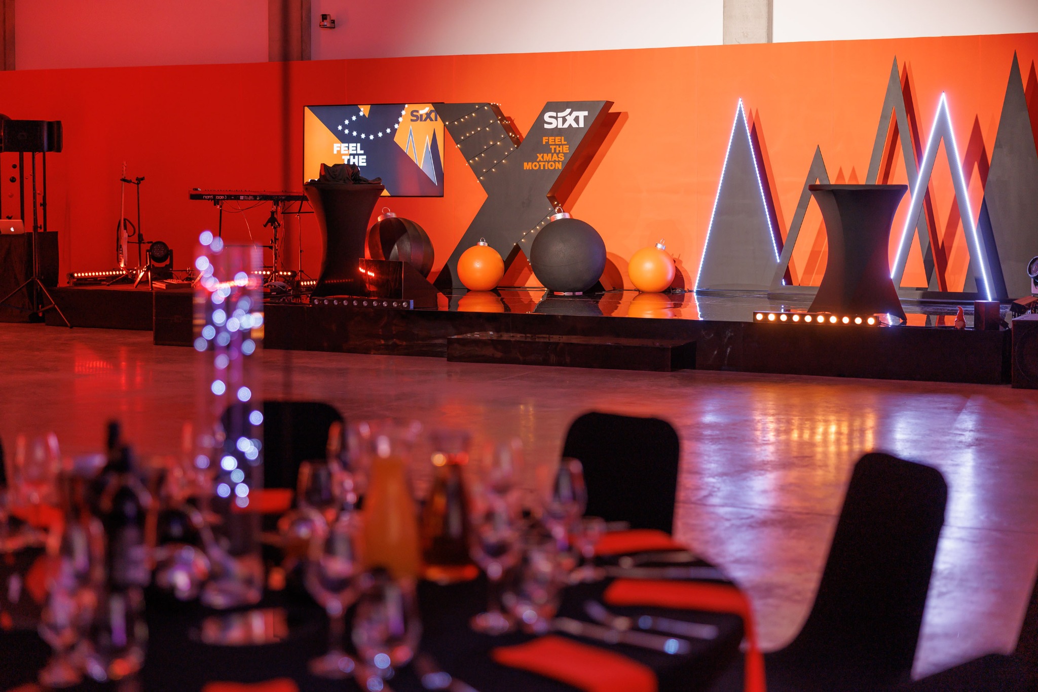 Scena z logo Sixt, świątecznymi dekoracjami i stołami nakrytymi na imprezę firmową w odcieniach czerwieni i czerni.