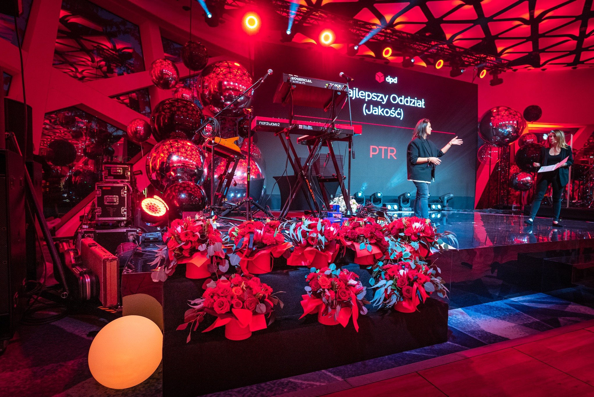 Scena z dekoracjami kwiatowymi i kulami dyskotekowymi w Warszawie, przygotowana na galę wręczenia nagród. Na scenie dwie osoby.