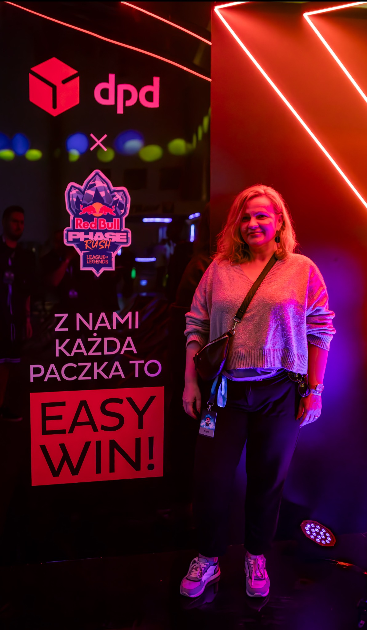 Kobieta na tle stoiska DPD Polska na Red Bull Phase Rush League of Legends z neonami i hasłem 'Z nami każda paczka to EASY WIN!'.