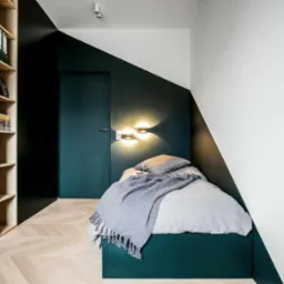 Nowoczesna aranżacja pokoju z pojedynczym ł&oacute;żkiem, szafą w zabudowie i parkietem w jodełkę; ściany w kolorze butelkowej zieleni kontrastują z bielą, a oświetlenie punktowe podkreśla minimalistyczny...