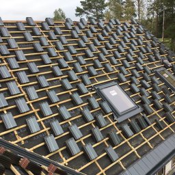 Dąb dach Paweł Dubicki - Montaż dachówki ceramicznej w Białymstoku, widok z góry na częściowo pokryty dach z trzema oknami dachowymi, dachówka w kolorze grafitowym ułożona na łatach.