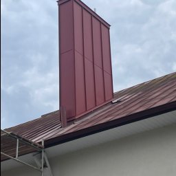 Dąb dach Paweł Dubicki - Nowoczesny, bordowy komin z blachy na dachu z dachówki ceramicznej. Widoczne fragmenty rusztowania i orynnowania. Pochmurne niebo w tle.