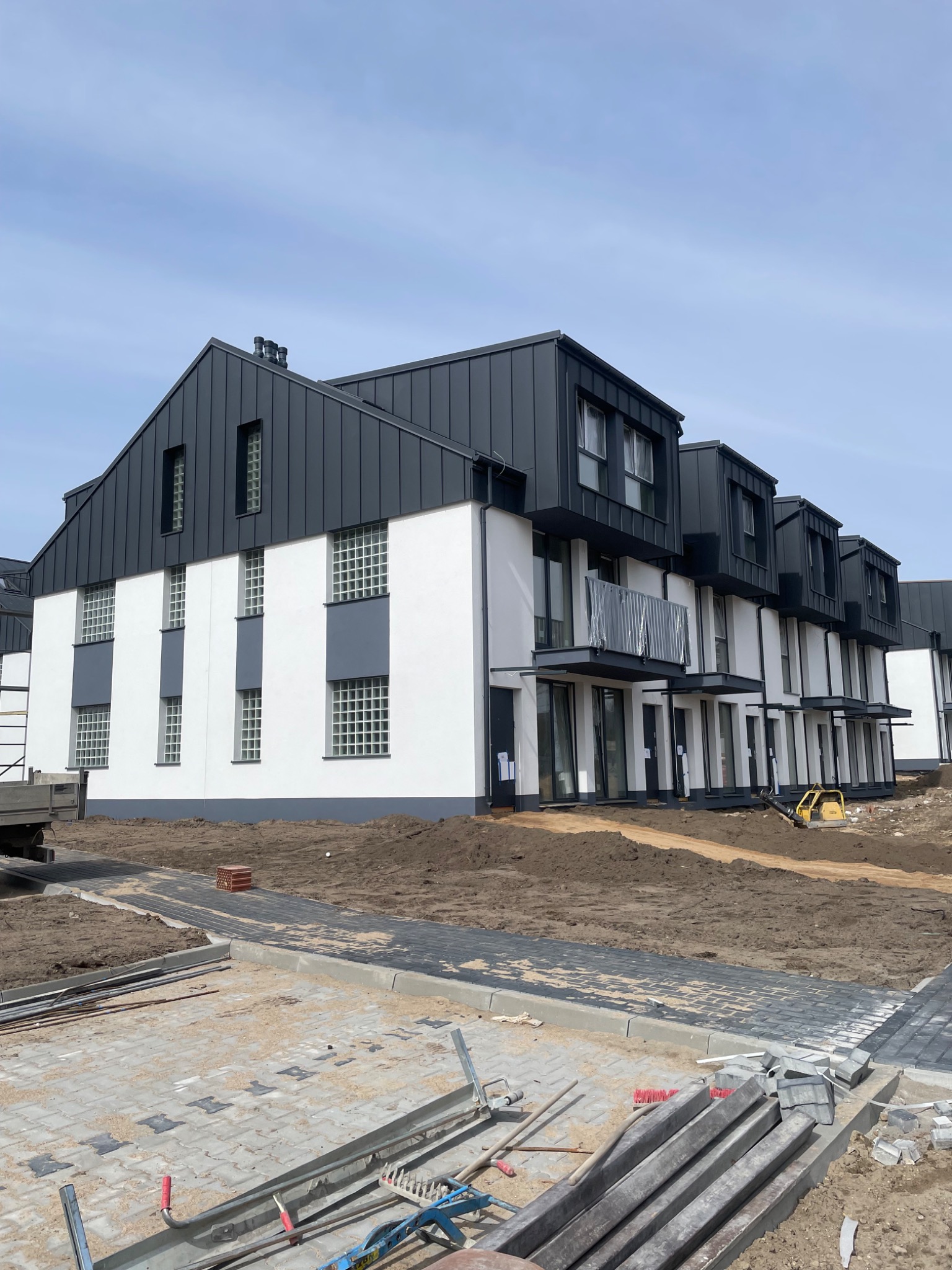 Nowoczesne budynki z ciemnymi dachami z blachy na etapie wykończenia, widoczne narzędzia i materiały budowlane.