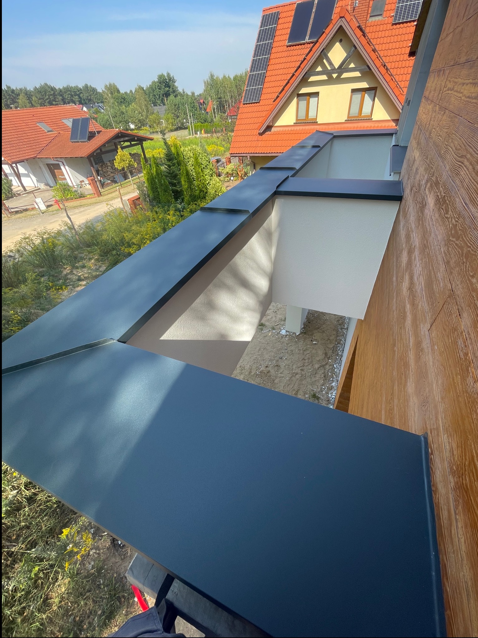 Nowoczesna, grafitowa obróbka blacharska dachu z widokiem na dom z panelami solarnymi w słoneczny dzień. Szczegółowe wykończenie krawędzi dachu.