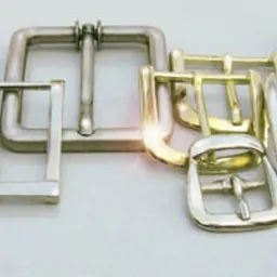 Kolekcja różnorodnych metalowych sprzączek do pasków, w tym modele z kryształkami, w odcieniach srebra, złota i czerni, ułożonych na gładkiej, jasnej powierzchni.