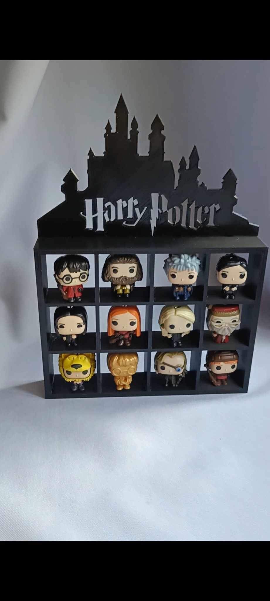 Czarny, drewniany regał z motywem Hogwartu i napisem Harry Potter, wypełniony kolekcjonerskimi figurkami Funko Pop przedstawiającymi postacie z sagi Harry Potter.