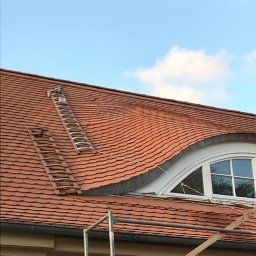 CARBUD - Ceglasty dach z dachówki karpiówki w Tczewie, dwie drabiny opierają się o połać, widoczne rusztowanie i okno na poddaszu.