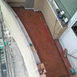 Układanie brązowych płytek ceramicznych na balkonie z widocznymi krzyżykami dystansowymi, poziomica i karton z zapasem płytek.