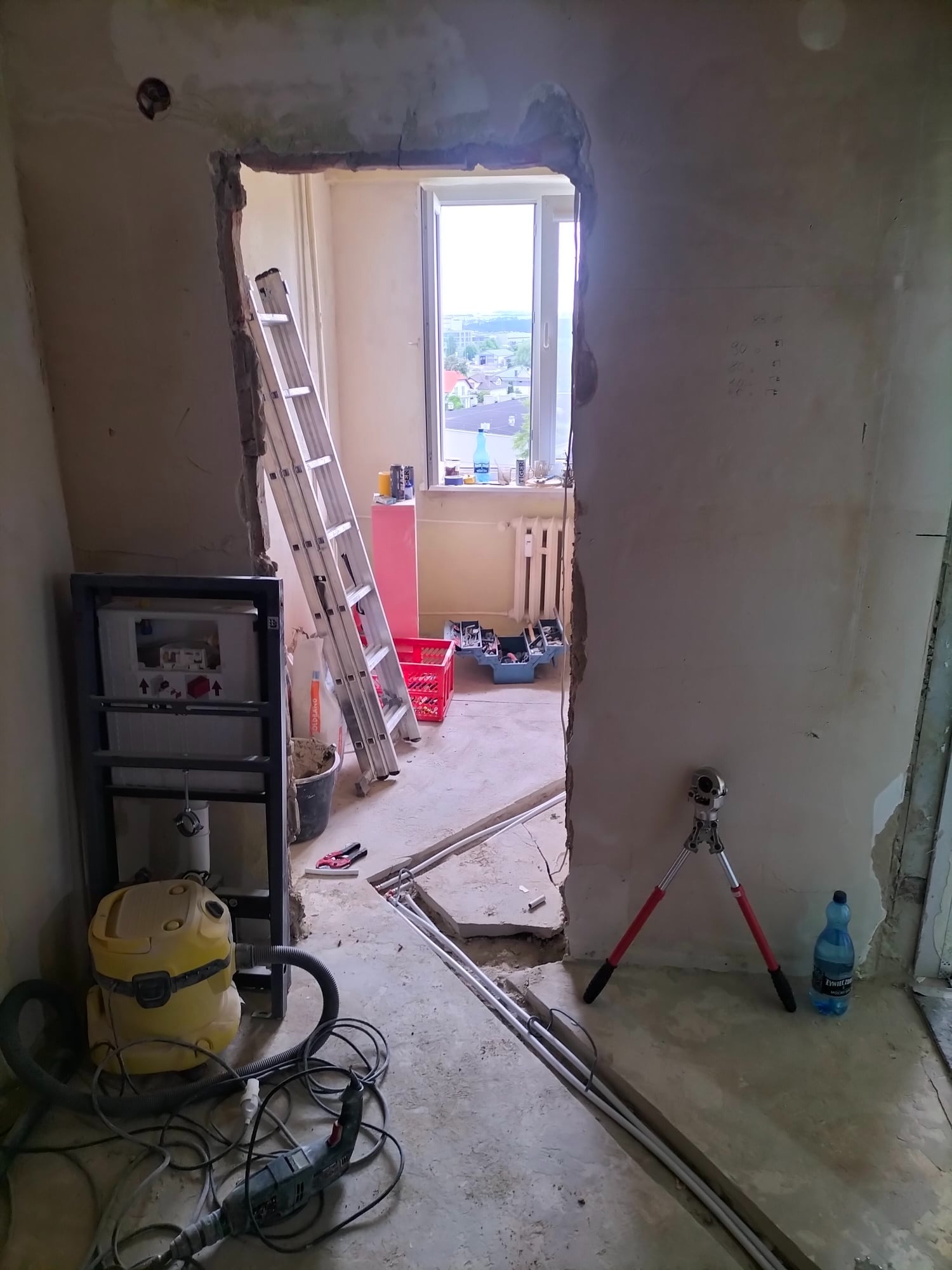 Wnętrze w trakcie remontu: widoczne rury w bruzdach, drabina oparta o ścianę, narzędzia i przybory budowlane, surowe ściany w trakcie prac wykończeniowych.