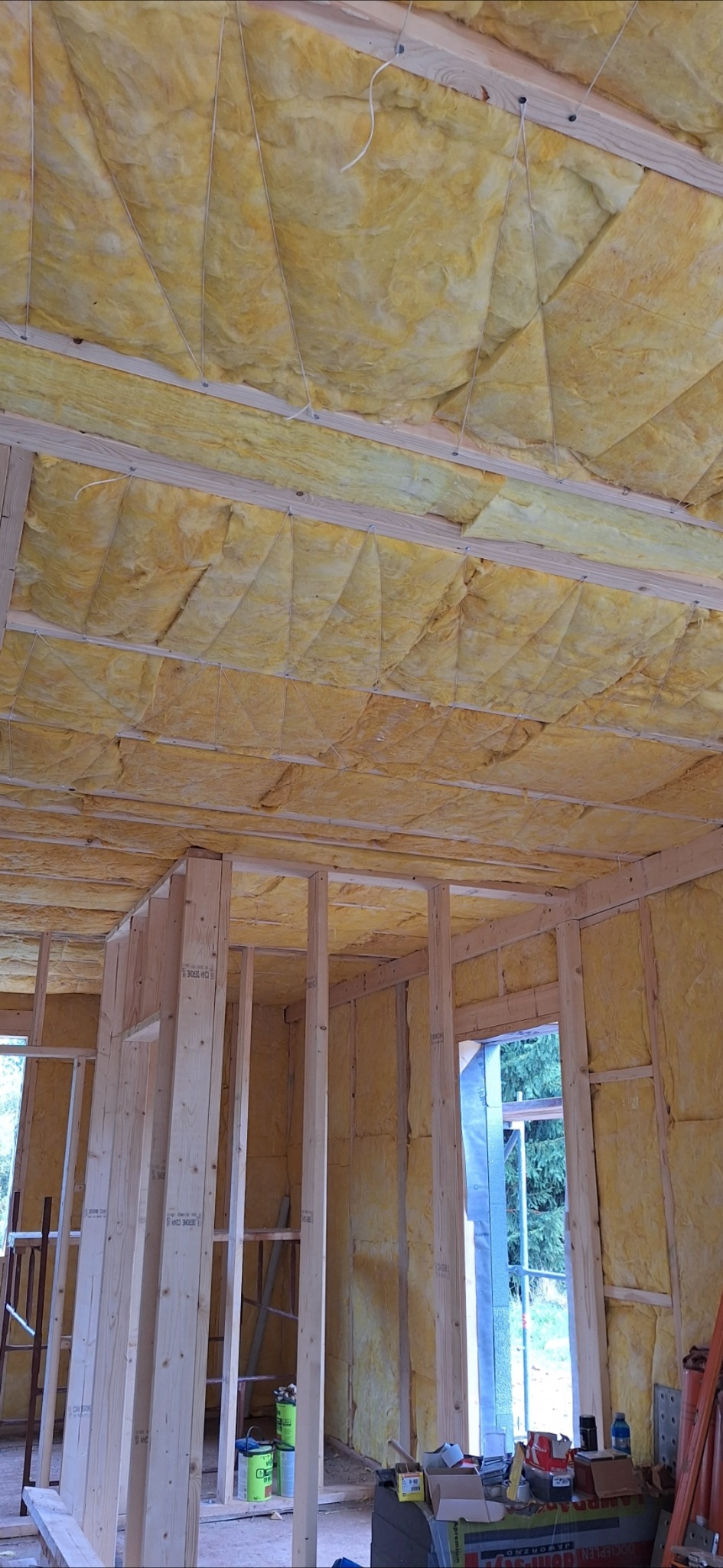 Wnętrze domu w trakcie budowy, ocieplone wełną mineralną, widoczne drewniane elementy konstrukcyjne ścian i sufitu. Ocieplenie przymocowane sznurkami.