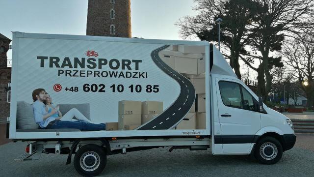 Biały samochód dostawczy z grafiką przedstawiającą parę siedzącą na kanapie i kartony, na tle wieży. Na boku pojazdu widnieje napis 'TRANSPORT Przeprowadzki' oraz numer telefonu.