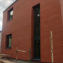 Usługi remontowo budowlane Mykola Dmytryk - Czerwona ceglana elewacja budynku z zamontowanymi oknami, widoczne rusztowania i materiały budowlane w trakcie prac wykończeniowych.