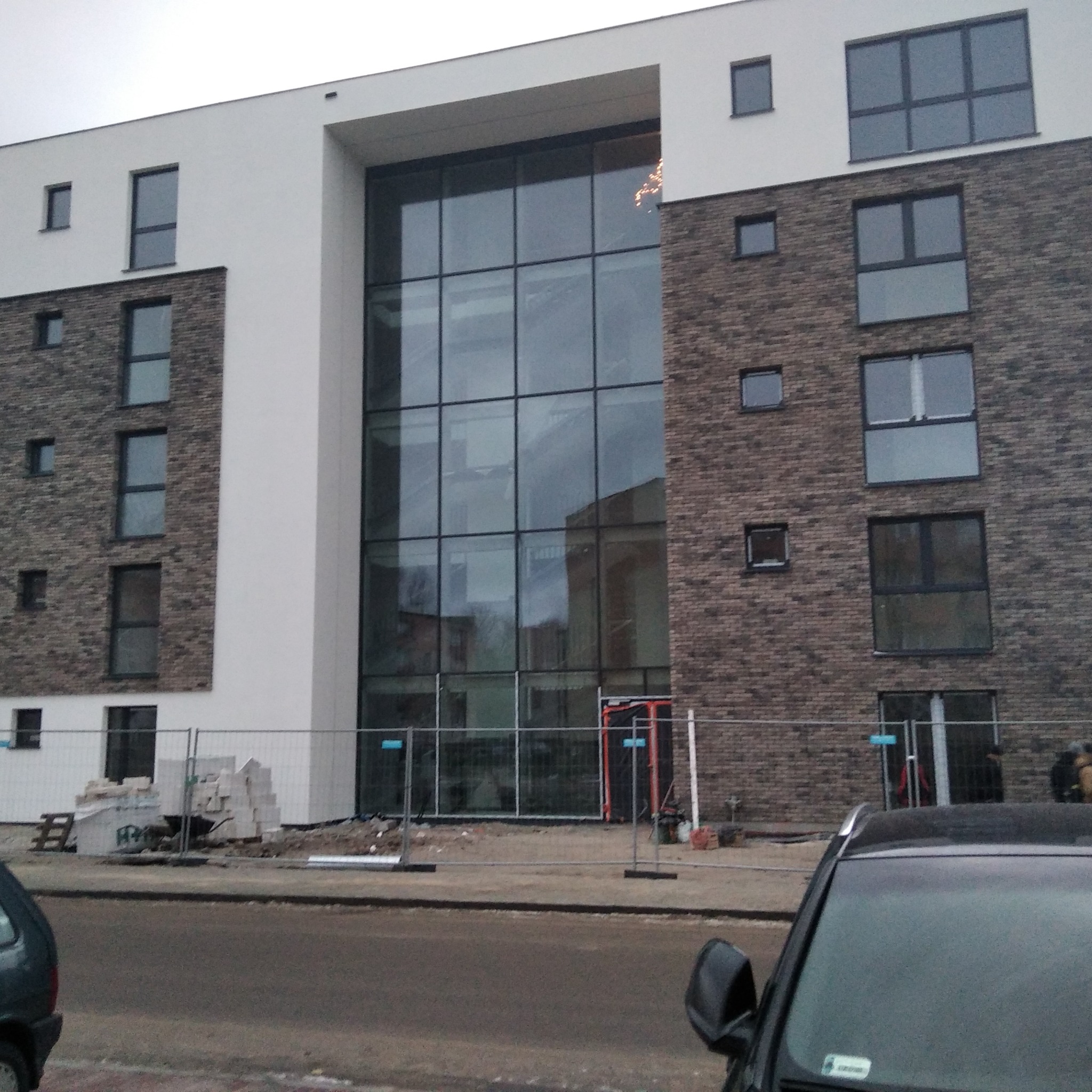 Budynek w trakcie budowy lub remontu elewacji, widoczne rusztowania i materiały budowlane przed budynkiem.