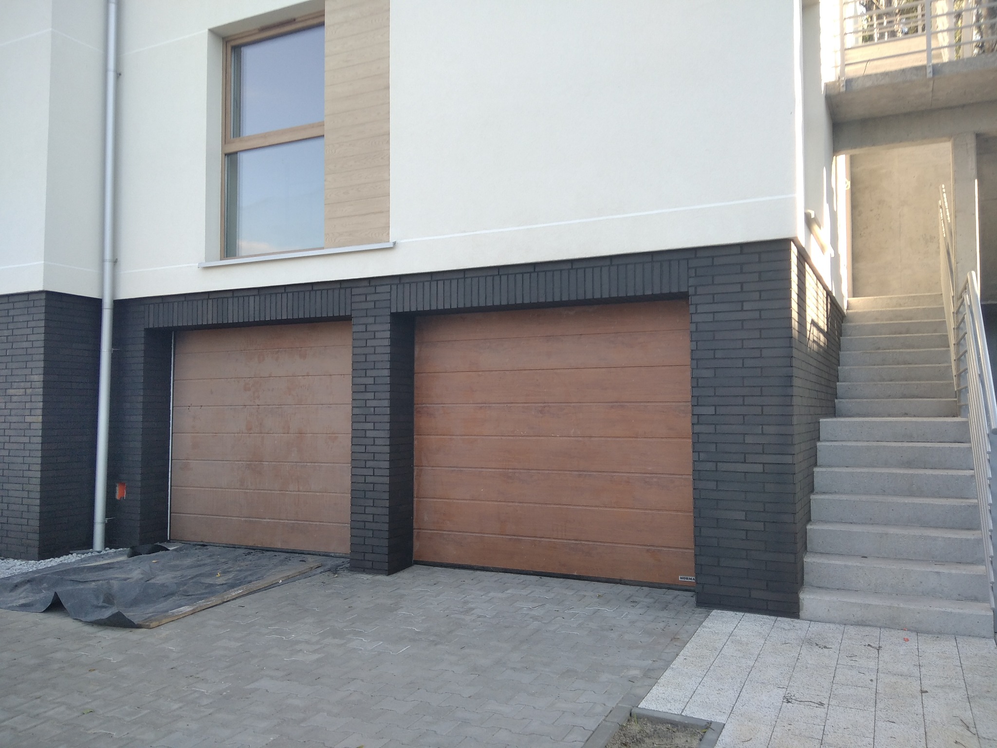 Dwa brązowe garaże segmentowe z czarną cegłą elewacyjną, widok z zewnątrz, betonowe schody obok.