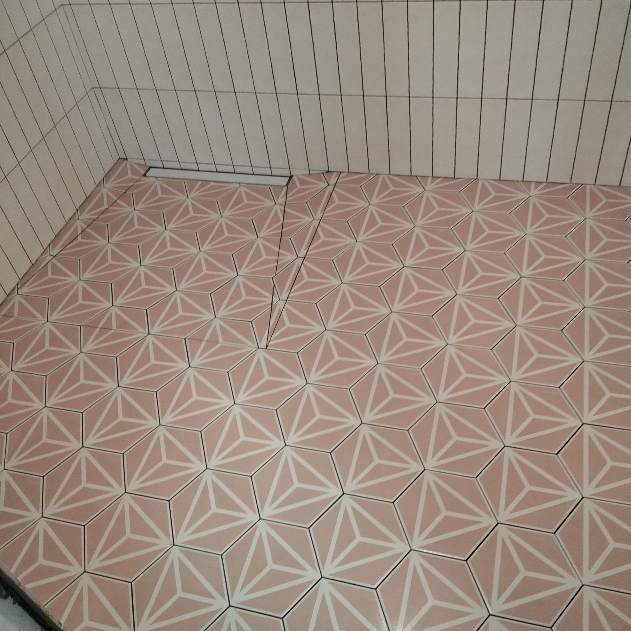 Wykończona łazienka z jasnoróżowymi, heksagonalnymi płytkami podłogowymi z geometrycznym wzorem i wąskimi, pionowymi białymi płytkami ściennymi z czarnymi fugami.