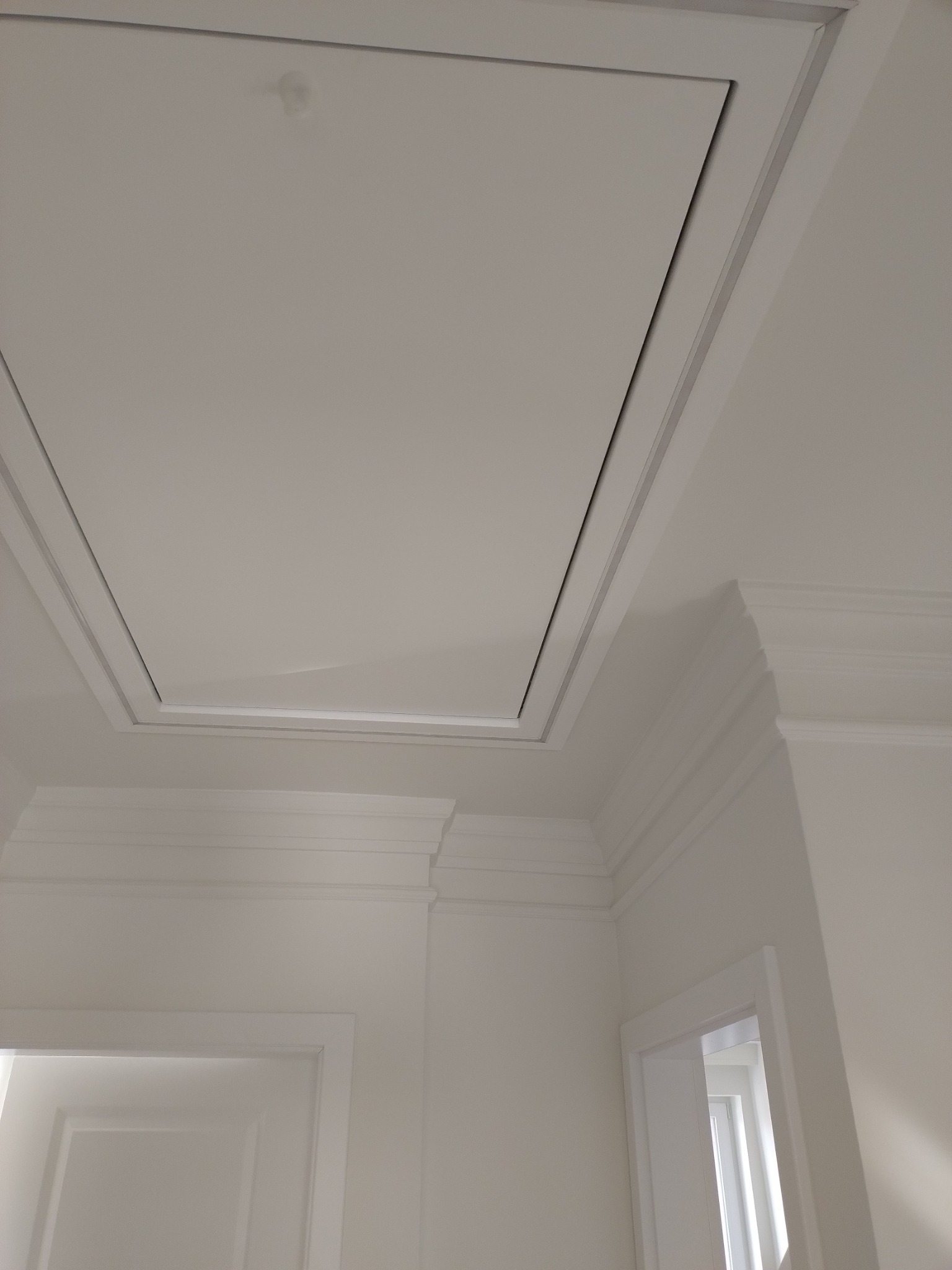 Biały sufit z klapą rewizyjną i ozdobnymi listwami w Rumi, widok z dołu.