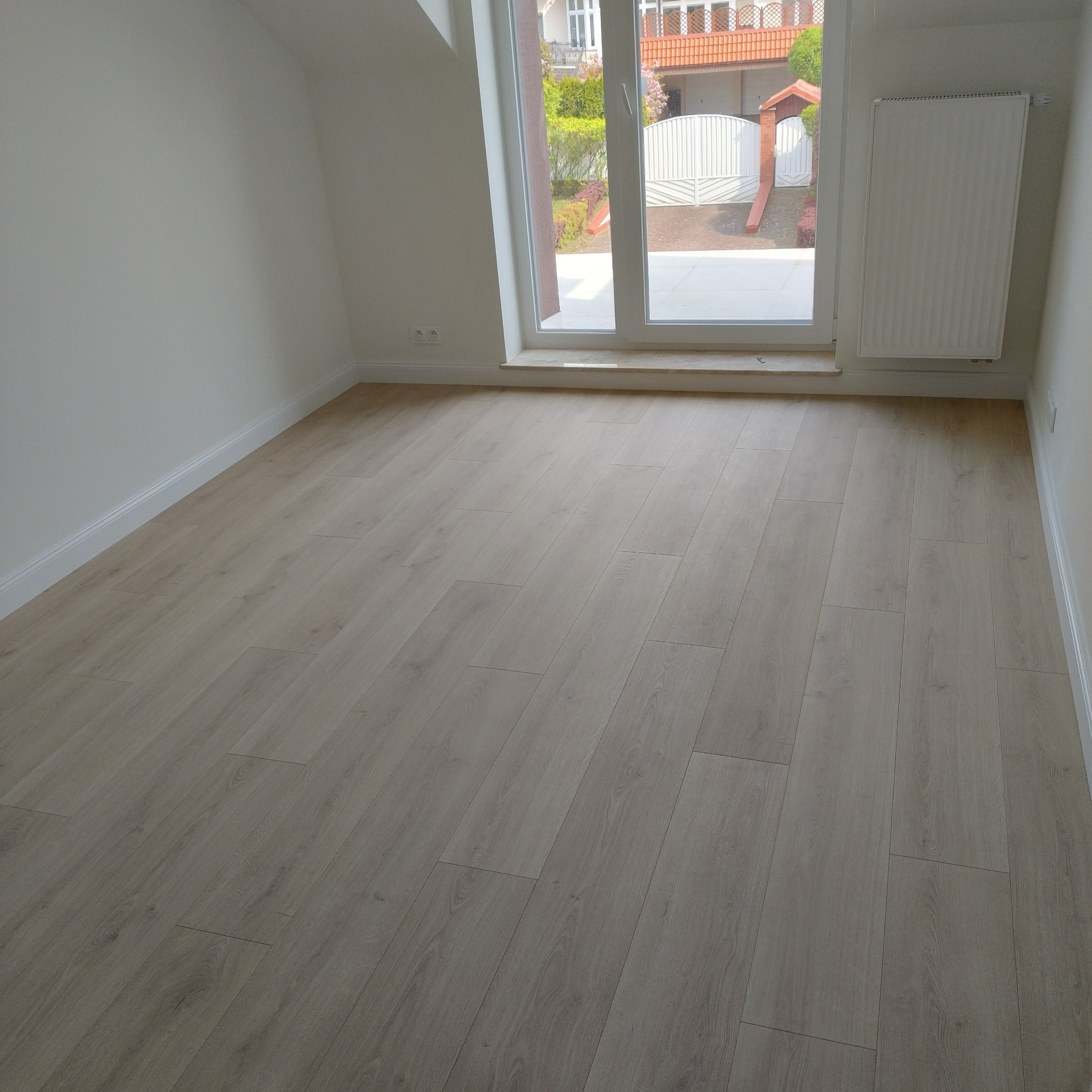 Jasne panele podłogowe ułożone w nowym pokoju na poddaszu z oknem i grzejnikiem.