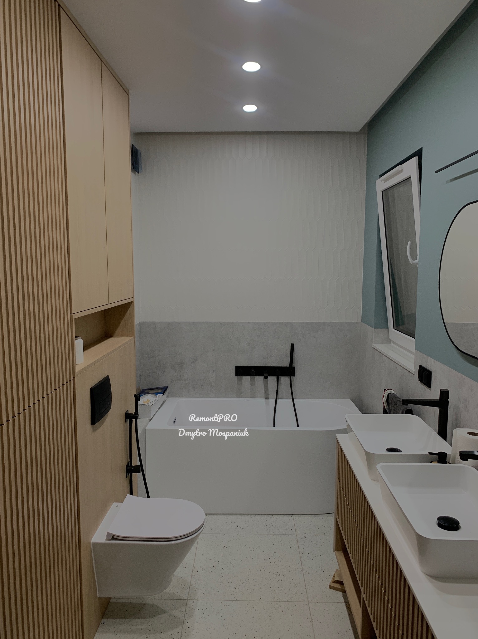 Nowoczesna łazienka z wanną, podwieszaną toaletą i dwiema umywalkami nablatowymi na szafce z lamelami, oświetlona punktowymi lampami sufitowymi.