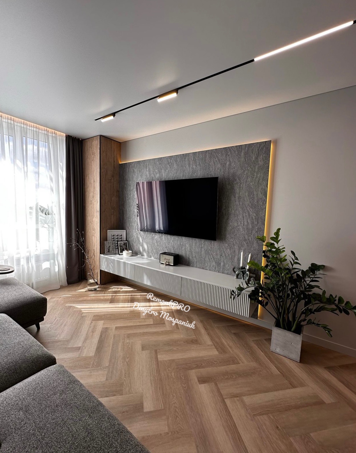 Nowoczesny salon z parkietem w jodełkę, szarą ścianą z telewizorem, podświetleniem LED i minimalistyczną szafką RTV.