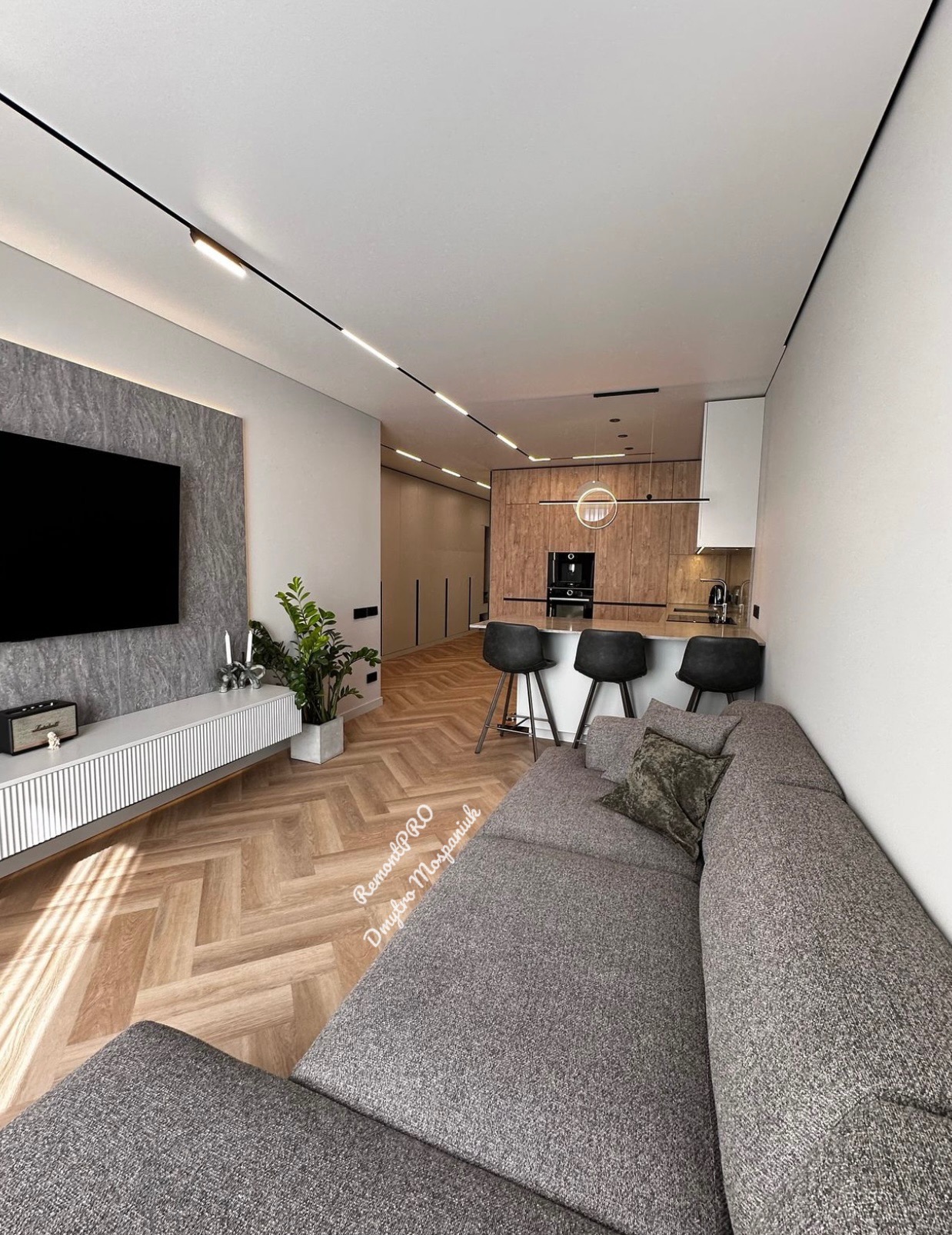Nowoczesne wnętrze z parkietem w jodełkę, szarą sofą narożną, ścianą TV z imitacją kamienia i oświetleniem liniowym LED.