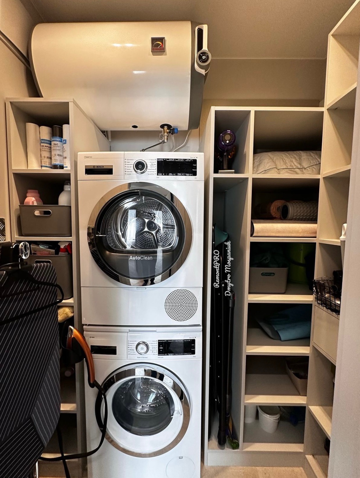 Pralka i suszarka Bosch w zabudowie meblowej, obok regał z półkami, na ścianie bojler, widoczne akcesoria do sprzątania.