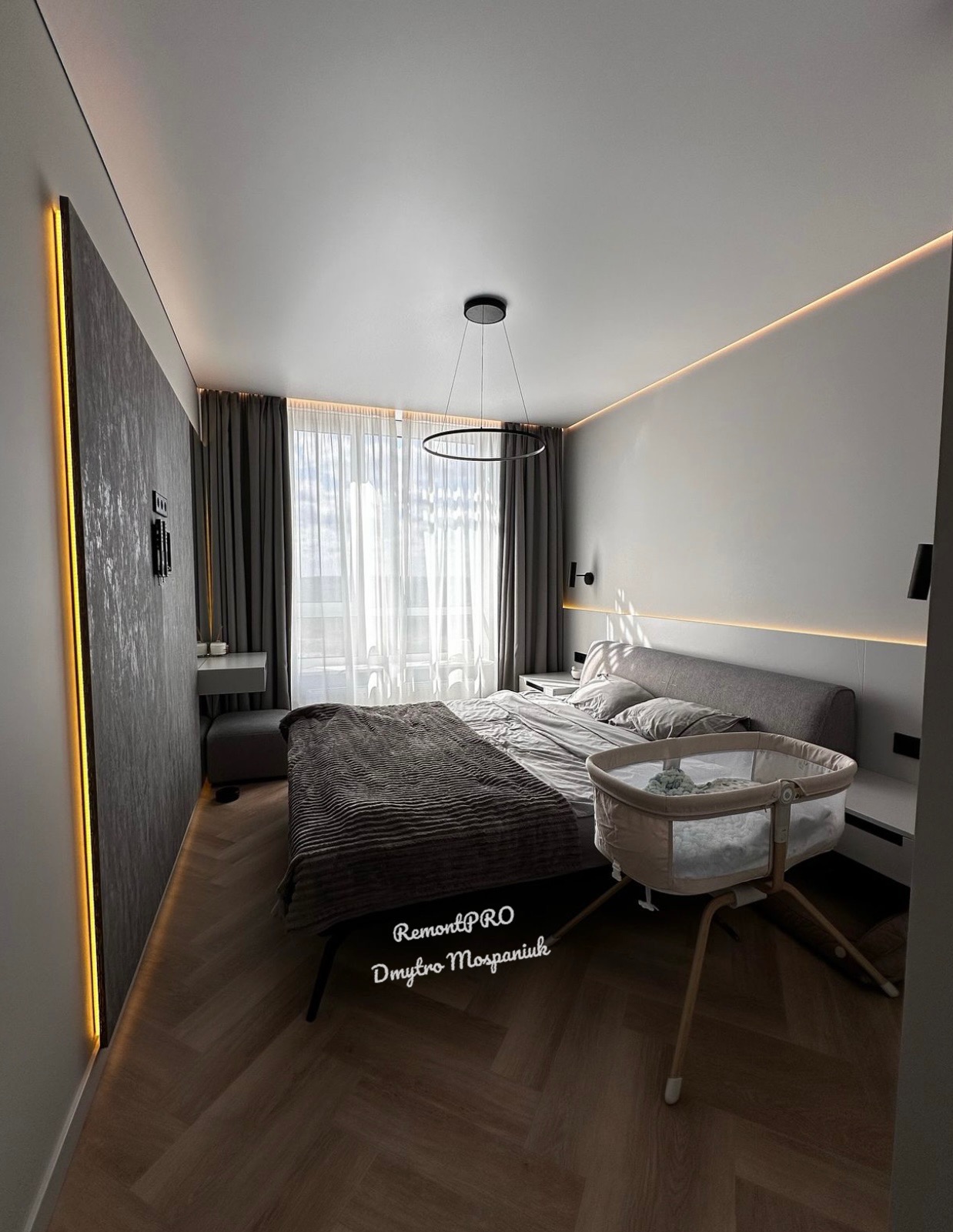 Nowoczesna sypialnia w odcieniach szarości z łóżeczkiem niemowlęcym, oświetleniem LED na ścianach i suficie oraz podłogą ułożoną w jodełkę.