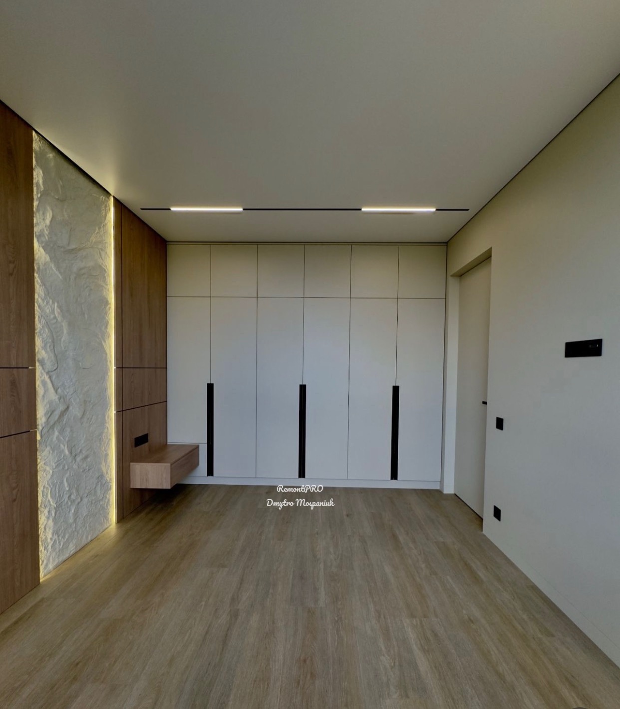 Nowoczesna sypialnia z podświetlaną ścianą z imitacji kamienia, zabudową meblową w kolorze bieli z czarnymi uchwytami i drewnianą podłogą panelową.