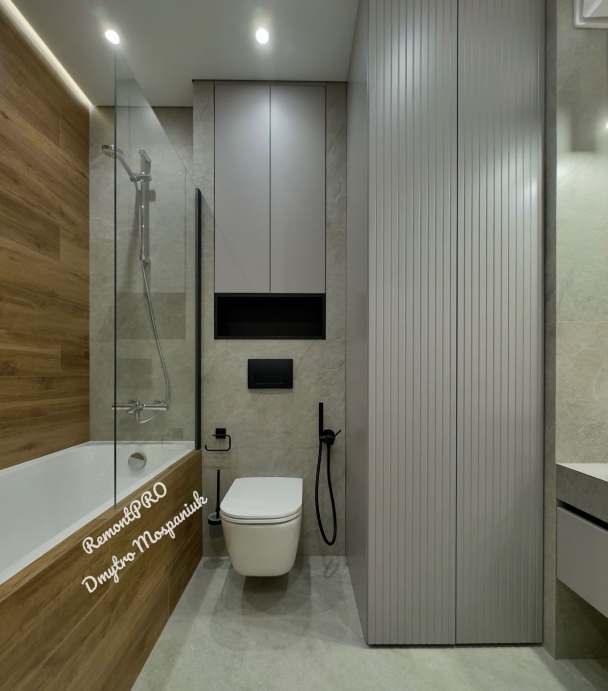 Nowoczesna łazienka z drewnianą obudową wanny, szklanym panelem prysznicowym, wiszącą toaletą z czarnym uchwytem na papier toaletowy i szarymi szafkami z pionowymi żłobieniami.