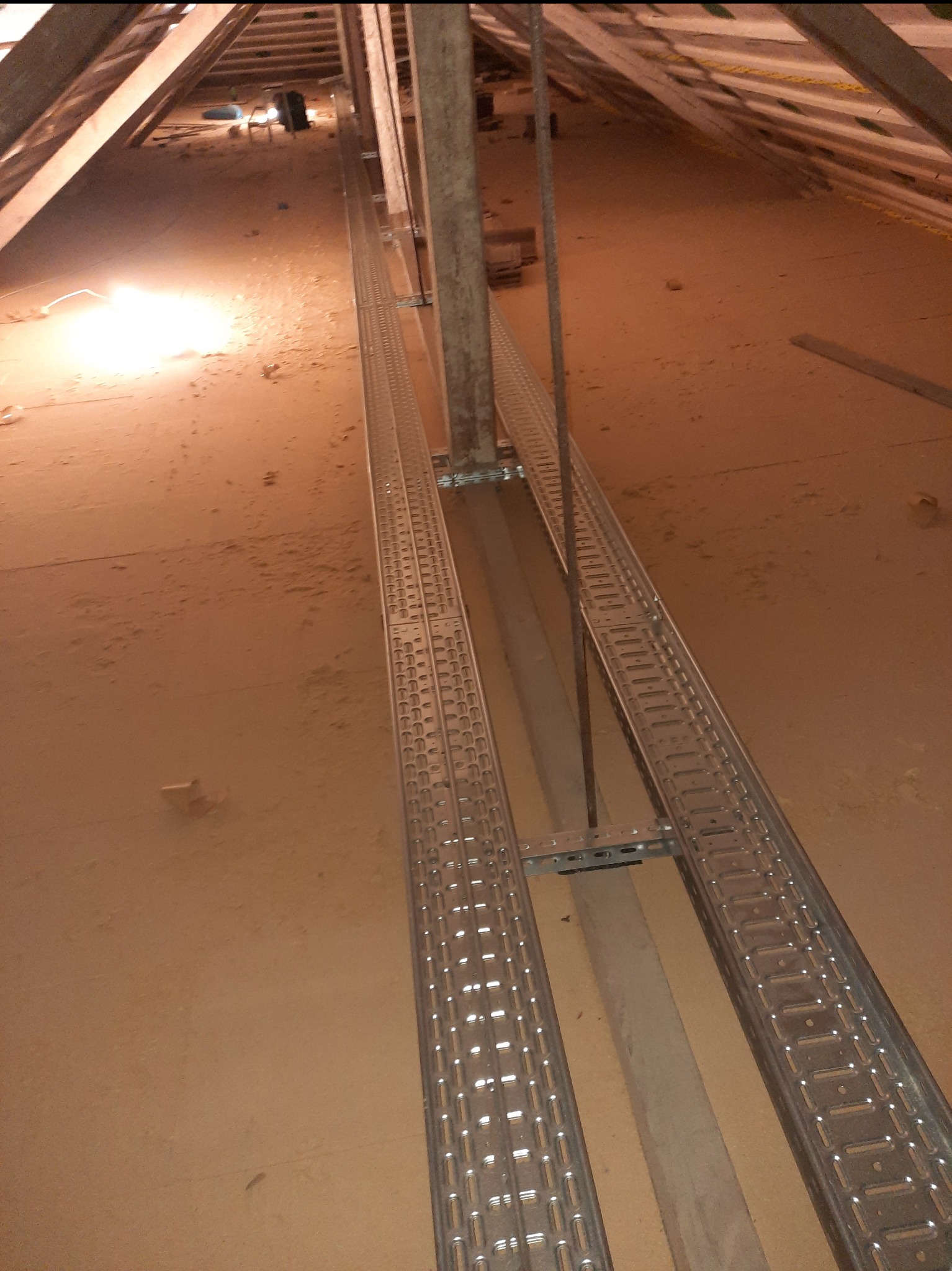 Metalowe korytka kablowe zamontowane w przestrzeni poddasza, widoczne elementy konstrukcji dachu i izolacji.