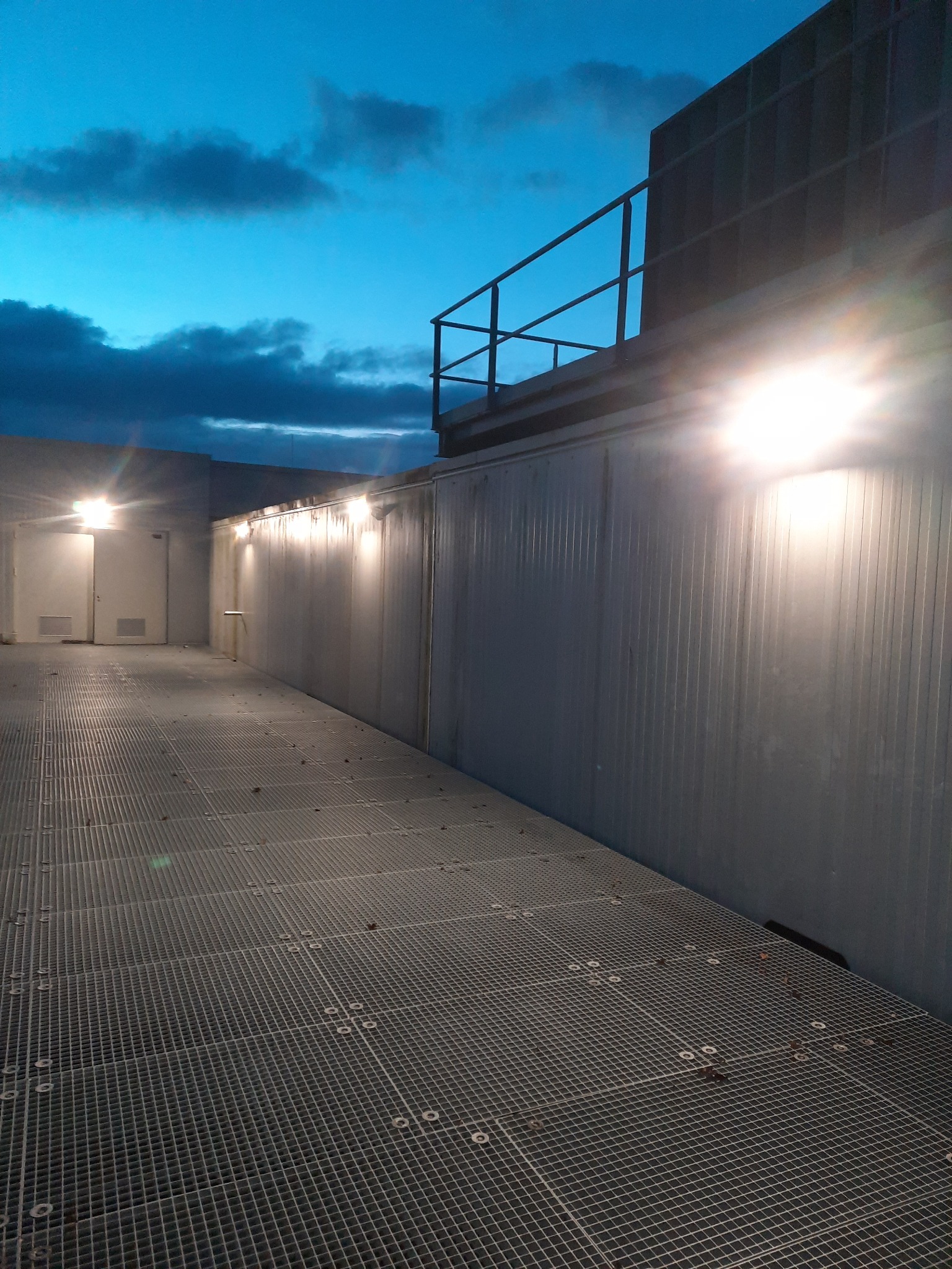 Zewnętrzne oświetlenie przemysłowe na metalowej konstrukcji z kratownicą podłogową, widok nocny z zachmurzonym niebem.