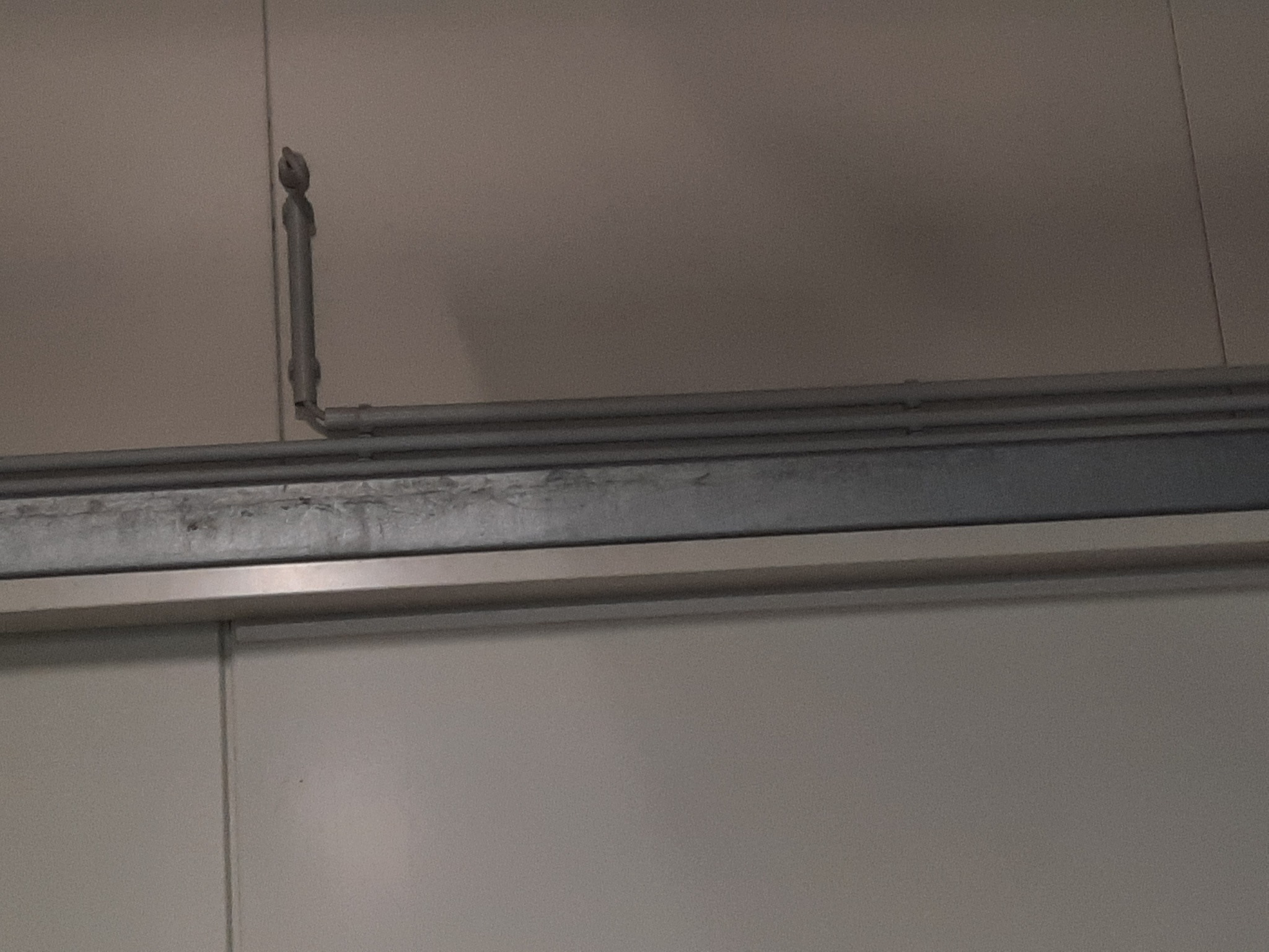 Szara rura instalacji odgromowej przymocowana do ściany, widoczne łączenia i element mocujący.