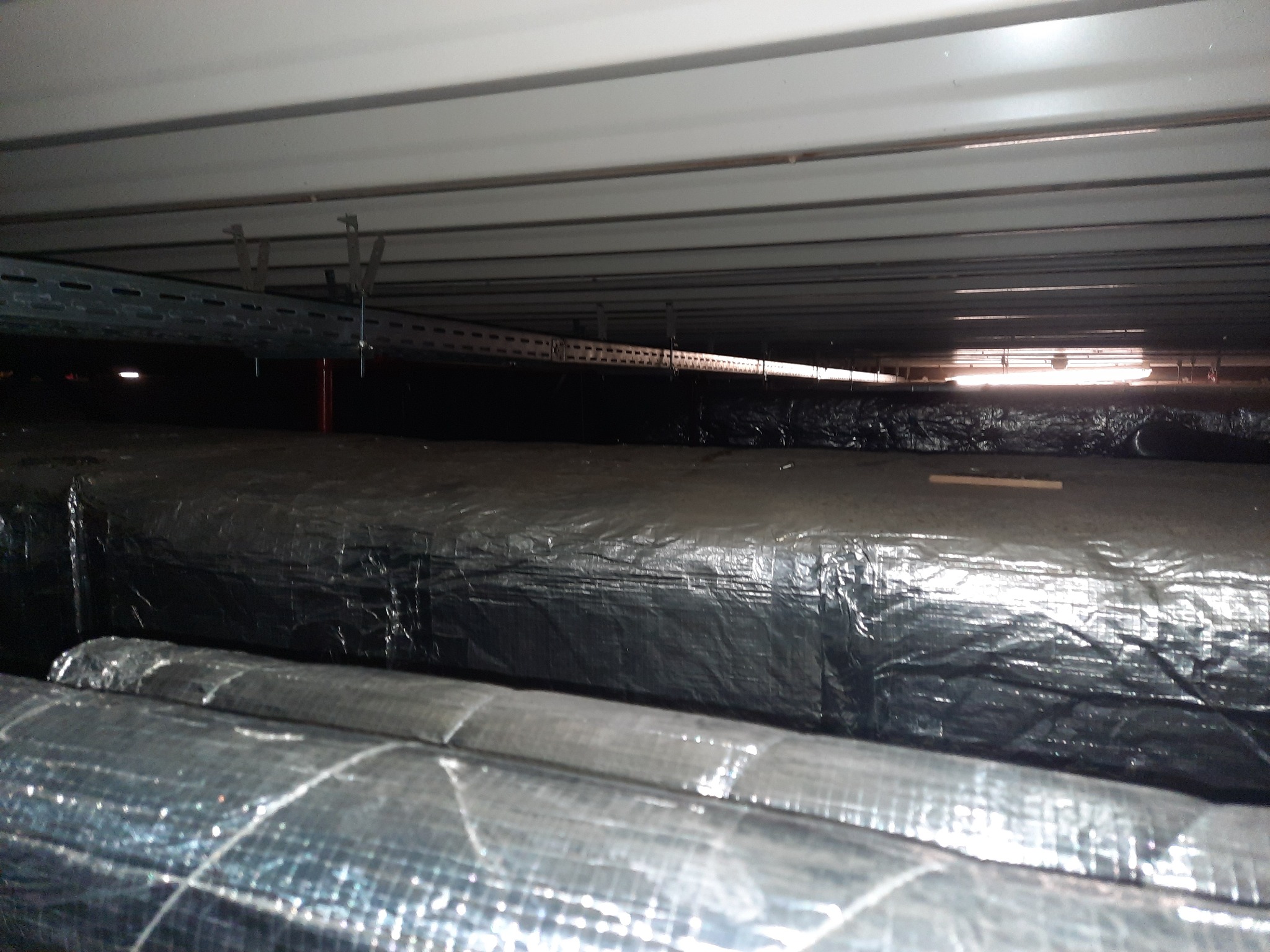 Izolowane rury pod sufitem, widoczne metalowe korytka kablowe pod stropem.