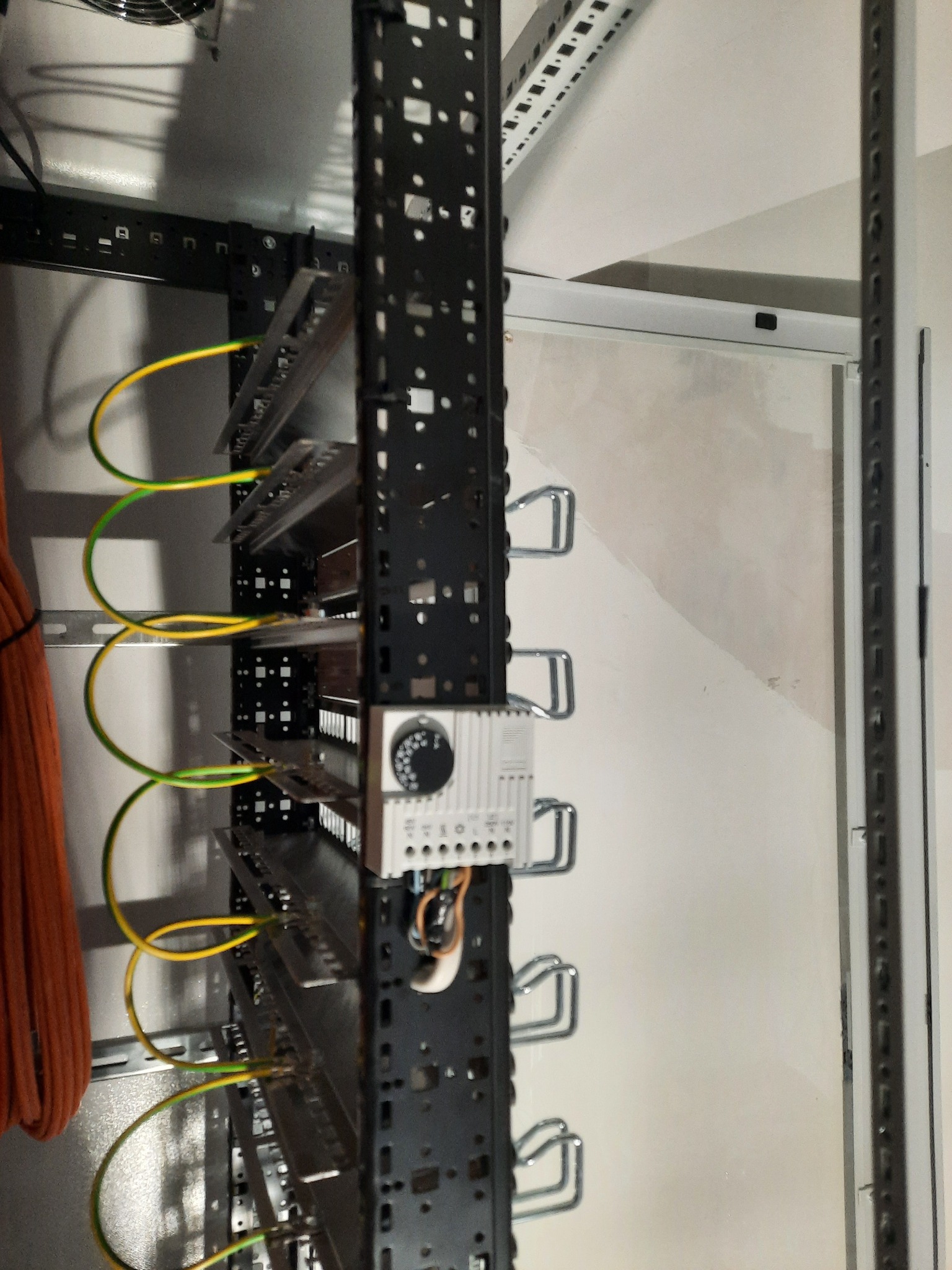 Szyna DIN z zamontowanymi zabezpieczeniami i przewodami ochronnymi w kolorach żółto-zielonym, widoczna w szafie elektrycznej.