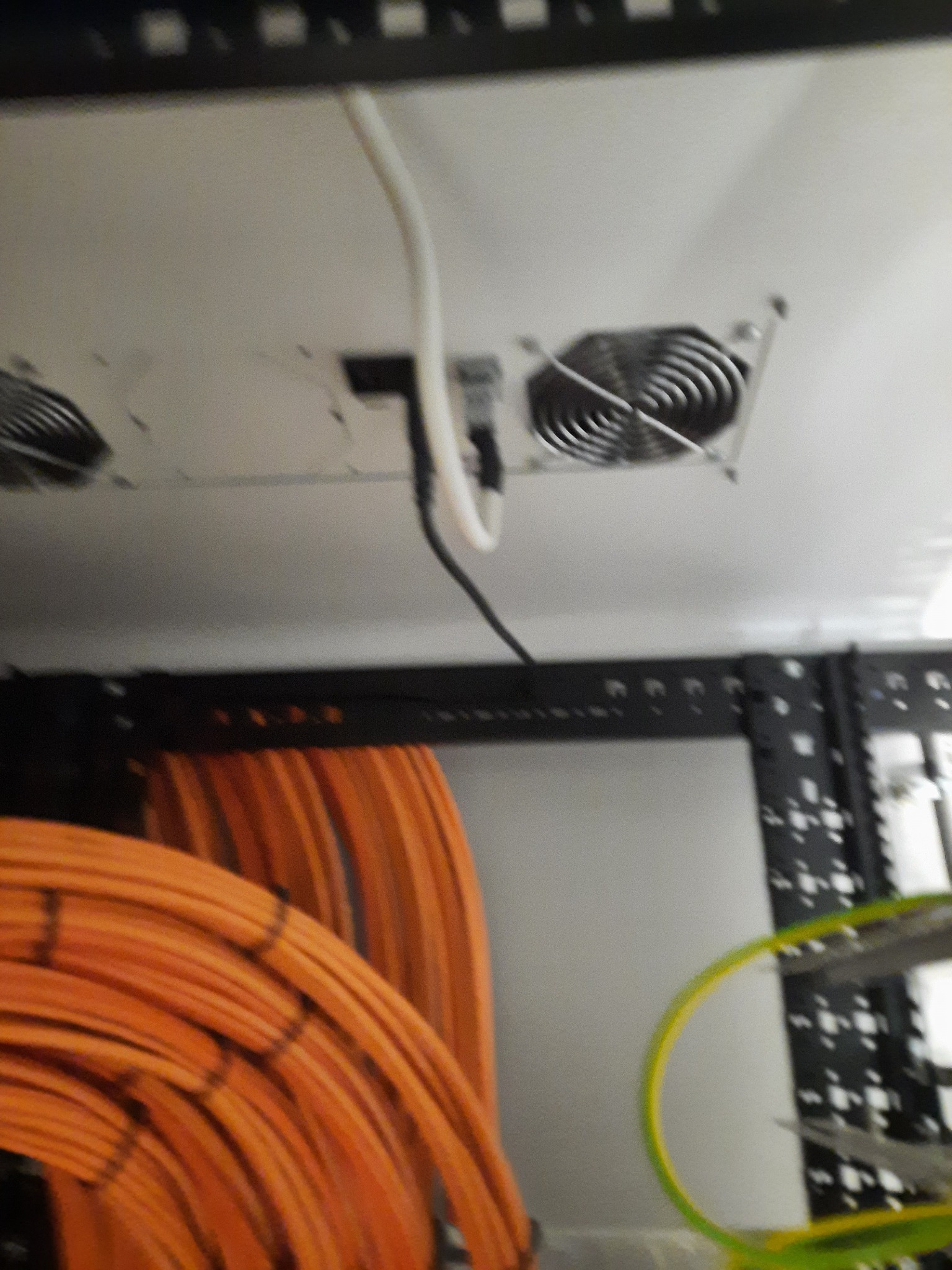 Fragment serwerowni z pomarańczowymi kablami ułożonymi w wiązki, widoczne wentylatory chłodzące zamontowane w suficie i fragment metalowej konstrukcji rack.