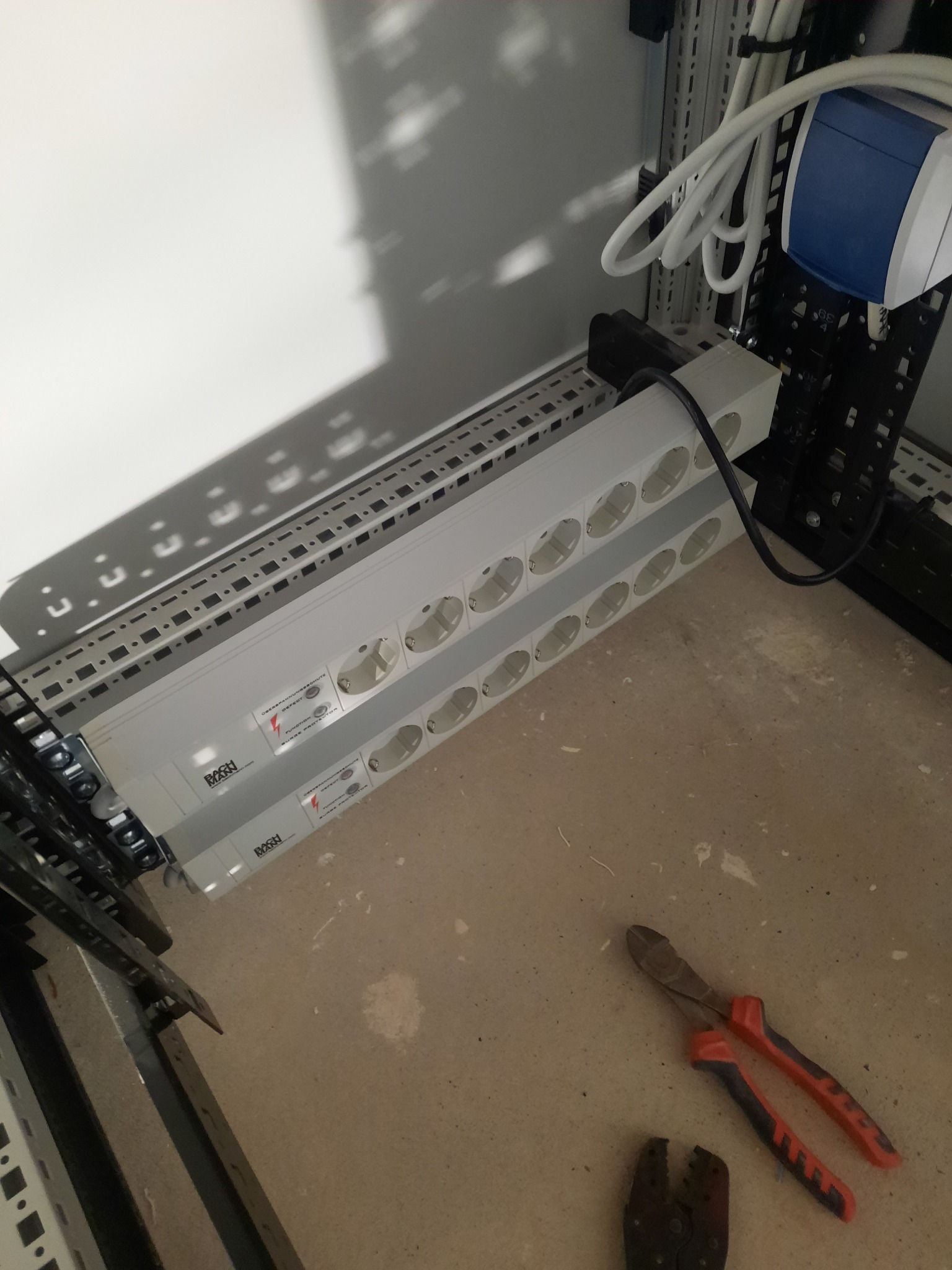 Dwa poziome, białe, wielogniazdkowe panele zasilające Bachmann zamontowane w szafie rack, widoczne narzędzia: obcinaczki i zaciskarka.